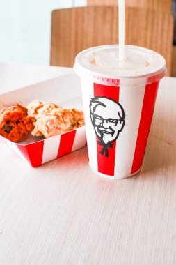 Bangkok, Tayland - 07 Ocak 2024 - Kağıt tabakta iki parça KFC kızarmış tavuk ve bir KFC restoranının içindeki masada üzerinde KFC logosu olan bir meşrubat bardağı.