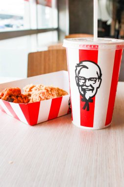 Bangkok, Tayland - 07 Ocak 2024 - Kağıt tabakta iki parça KFC kızarmış tavuk ve bir KFC restoranının içindeki masada üzerinde KFC logosu olan bir meşrubat bardağı.
