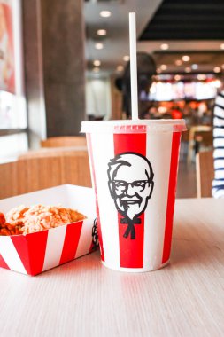 Bangkok, Tayland - 07 Ocak 2024 - Kağıt tabakta iki parça KFC kızarmış tavuk ve bir KFC restoranının içindeki masada üzerinde KFC logosu olan bir meşrubat bardağı.