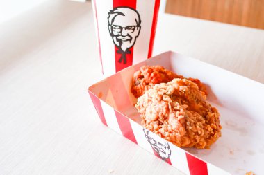 Bangkok, Tayland - 07 Ocak 2024 - Kağıt tabakta iki parça KFC kızarmış tavuk ve bir KFC restoranının içindeki masada üzerinde KFC logosu olan bir meşrubat bardağı.