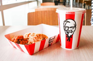 Bangkok, Tayland - 07 Ocak 2024 - Kağıt tabakta iki parça KFC kızarmış tavuk ve bir KFC restoranının içindeki masada üzerinde KFC logosu olan bir meşrubat bardağı.
