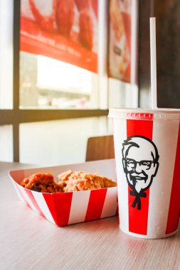 Bangkok, Tayland - 07 Ocak 2024 - Kağıt tabakta iki parça KFC kızarmış tavuk ve bir KFC restoranının içindeki masada üzerinde KFC logosu olan bir meşrubat bardağı.