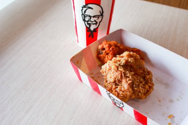 Bangkok, Tayland - 07 Ocak 2024 - Kağıt tabakta iki parça KFC kızarmış tavuk ve bir KFC restoranının içindeki masada üzerinde KFC logosu olan bir meşrubat bardağı.