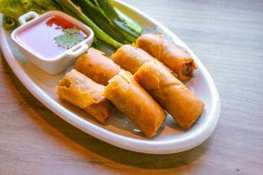 Taze kızartılmış altın sarısı börekler çeşitli sebzeler ve lezzetli bir sosla beyaz bir tabağa konur..