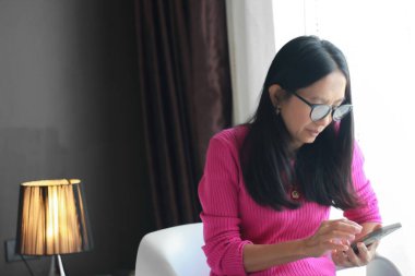 Evdeki oturma odasında akıllı telefon kullanan Asyalı kadın, yaşam tarzı konsepti..