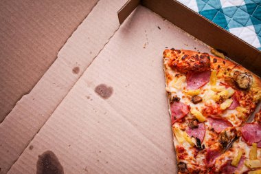 Yenen üç dilim pizza karton bir kutuda bırakıldı. Akçaağaç renkli ahşap bir masaya yerleştirilmiş. Ve yeşil ekose bir paspas..