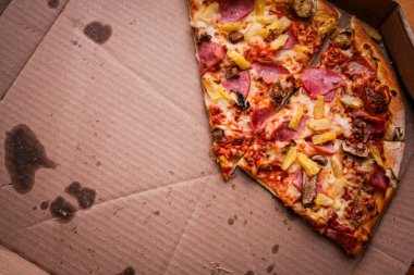 Yenen üç dilim pizza karton bir kutuda bırakıldı. Akçaağaç renkli ahşap bir masaya yerleştirilmiş. Ve yeşil ekose bir paspas..