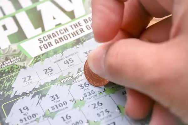 stock image Washington, USA - July 20 2024 - A man is hand erases a protective field in a lottery with a coin on a wooden background. Lotto, America, USA.