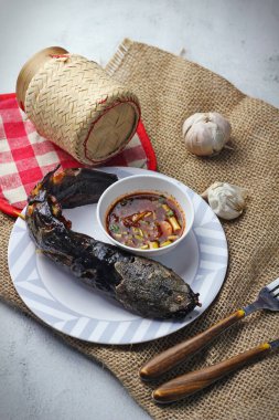 Bütün bir ızgara yayın balığı, yanında baharatlı sosla birlikte rustik bir tabakta servis edilir. Balığın kıtır kıtır, altın sarısı bir teni vardır ve çuval bezinden bir yatağa yerleştirilir..