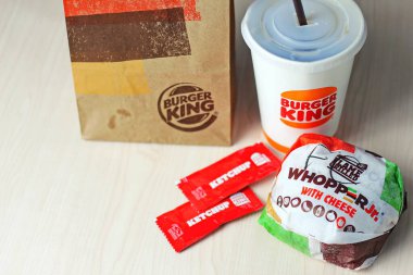 WASHINGTON - ABD - 17 Ağustos 2024 - Klasik bir Burger King yemeği - Peynirli Whopper Jr. bir fincan soda, ketçap paketleri ve kahverengi bir kese kağıdı.