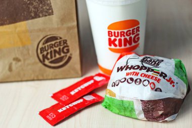 WASHINGTON - ABD - 17 Ağustos 2024 - Peynirli Whopper Jr. 'ın yakın çekimi, Burger King içeceği ve beyaz bir masada ketçap paketleri.
