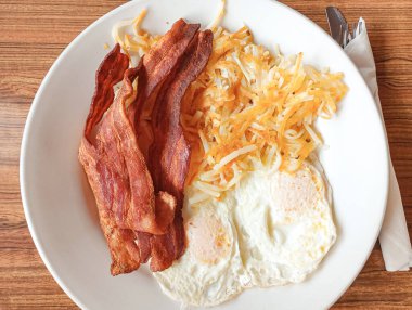 Altın-kahverengi mücver beyaz bir tabakta üst üste istiflenir. Çıtır pastırma şeritleri ve yanında mükemmel bir kızarmış yumurta bulunur. Görüntü, klasik bir Amerikan kahvaltısının rahatlatıcı kokusunu çağrıştırıyor.