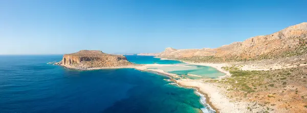 This landscape photo was taken, in Europe, in Greece, in Crete, in Balos, At the edge of the Mediterranean Sea, in summer. We see the fine sandy beach with pink reflections at the foot of the rocky cliffs, under the sun.