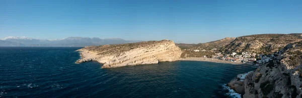 This landscape photo was taken, in Europe, in Greece, in Crete, in Matala, At the edge of the Mediterranean Sea, in summer. We see the panoramic view of the city center and its beach and cliffs, under the sun.