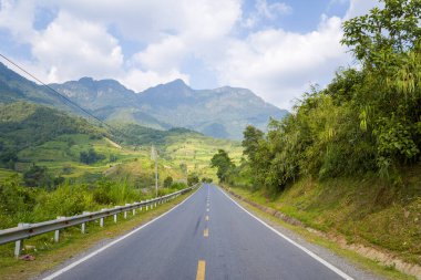Bu manzara fotoğrafı Asya 'da Vietnam' da, Tonkin 'de Lai Chau ve Sapa arasında yazın çekildi. Kırsal ve dağların ortasında asfalt bir yol görüyoruz. Güneşin altında..