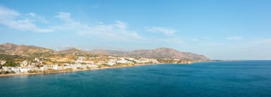 Bu manzara fotoğrafı, Avrupa 'da, Yunanistan' da, Girit 'te, Analipsi' de, Akdeniz 'in kıyısında, yazın çekildi. Dağların eteklerinde, güneşin altında kutsal sahili ve kumlu sahili görüyoruz..