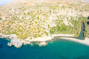 Bu manzara fotoğrafı Avrupa 'da, Yunanistan' da, Girit 'te, Preveli' de, Akdeniz kıyısında, yazın çekildi. Dağın eteğinde kumlu bir sahil görüyoruz. Güneşin altında, yeşil bir palmiye koruluğunun yanında..