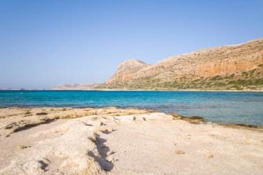 Bu manzara fotoğrafı Avrupa 'da, Yunanistan' da, Girit 'te, Balos' ta, Akdeniz 'in kıyısında, yazın çekildi. Kayalık kayalıkların dibinde, güneşin altında pembe yansımaları olan kumlu bir sahil görüyoruz..