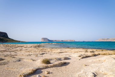 Bu manzara fotoğrafı Avrupa 'da, Yunanistan' da, Girit 'te, Balos' ta, Akdeniz 'in kıyısında, yazın çekildi. Kayalık kayalıkların dibinde, güneşin altında pembe yansımaları olan kumlu bir sahil görüyoruz..