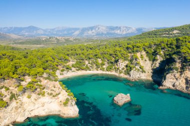 This landscape photo was taken, in Europe, in Greece, in Epirus, towards Igoumenitsa, at the edge of the Ionian Sea, in summer. We see the fine sandy beach of Alonaki Fanariou and its green rocky cliffs, under the sun. clipart