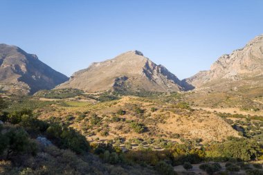 Bu manzara fotoğrafı Avrupa 'da, Yunanistan' da, Girit 'te, Preveli' ye doğru, Akdeniz kıyısında, yazın çekildi. Kırsalın ortasında, güneşin altında kurak ve kayalık dağlar görüyoruz..