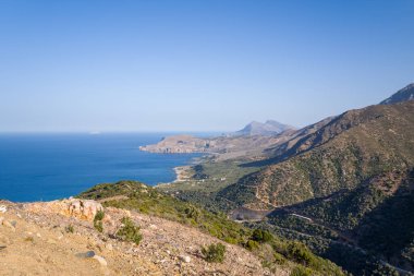 Bu manzara fotoğrafı Avrupa 'da, Yunanistan' da, Girit 'te, Chania' ya doğru, Akdeniz 'in kıyısında, yazın çekildi. Kayalık dağların eteklerinde, güneşin altında yeşil kırları görüyoruz..