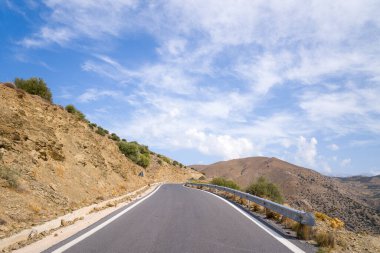 Bu manzara fotoğrafı Avrupa 'da, Yunanistan' da, Girit 'te, Tsoutsouros' a doğru, Akdeniz 'in kıyısında, yazın çekildi. Kurak bir yolda asfalt bir yol görüyoruz ama güneşin altında yeşil dağlar..