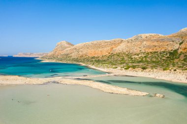 Bu manzara fotoğrafı Avrupa 'da, Yunanistan' da, Girit 'te, Balos' ta, Akdeniz 'in kıyısında, yazın çekildi. Kayalık kayalıkların dibinde, güneşin altında pembe yansımaları olan kumlu bir sahil görüyoruz..