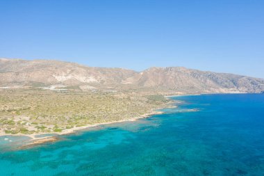 Bu manzara fotoğrafı Avrupa 'da, Yunanistan' da, Girit 'te, Elafonisi' de, Akdeniz kıyısında, yazın çekildi. Güneşin altında kayalık sahili ve kurak dağlarını görüyoruz..