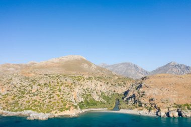 Bu manzara fotoğrafı Avrupa 'da, Yunanistan' da, Girit 'te, Preveli' de, Akdeniz kıyısında, yazın çekildi. Dağın eteğinde kumlu bir sahil görüyoruz. Güneşin altında, yeşil bir palmiye koruluğunun yanında..