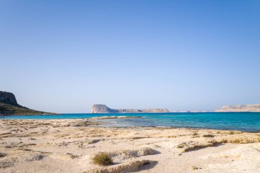 Bu manzara fotoğrafı Avrupa 'da, Yunanistan' da, Girit 'te, Balos' ta, Akdeniz 'in kıyısında, yazın çekildi. Kayalık kayalıkların dibinde, güneşin altında pembe yansımaları olan kumlu bir sahil görüyoruz..
