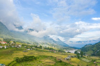 Bu manzara fotoğrafı Asya 'da, Vietnam' da, Tonkin 'de, Sapa' da Lao Cai 'de, yazın çekildi. Yeşil ve sarı pirinç tarlalarıyla geleneksel köyü görüyoruz. Yeşil dağlarda, bulutların altında..