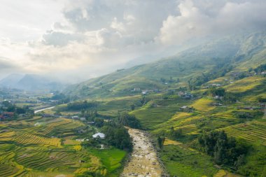 Bu manzara fotoğrafı Asya 'da, Vietnam' da, Tonkin 'de, Sapa' da Lao Cai 'de, yazın çekildi. Yeşil ve sarı pirinç tarlalarıyla geleneksel köyü görüyoruz. Yeşil dağlarda, bulutların altında..
