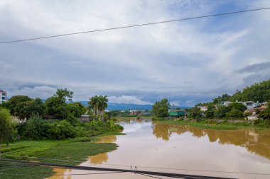 Bu manzara fotoğrafı Asya 'da, Vietnam' da, Tonkin 'de, Dien Bien Phu' da, yazın çekildi. Şehrin ortasında güneşin altında ağaçlarla kaplı Nam Rom Nehri 'ni görüyoruz..