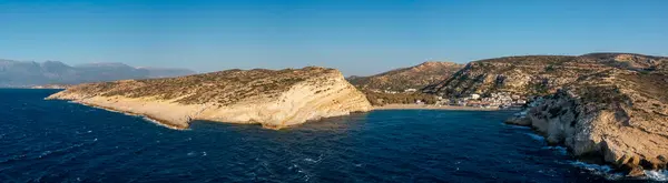 This landscape photo was taken, in Europe, in Greece, in Crete, in Matala, At the edge of the Mediterranean Sea, in summer. We see the panoramic view of the city center and its beach and cliffs, under the sun.