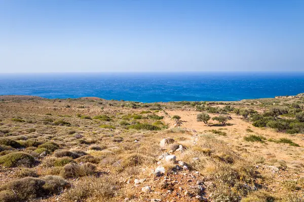 This landscape photo was taken, in Europe, in Greece, in Crete, towards Matala, At the edge of the Mediterranean Sea, in summer. We see the arid rocky coast and its green countryside, under the sun.