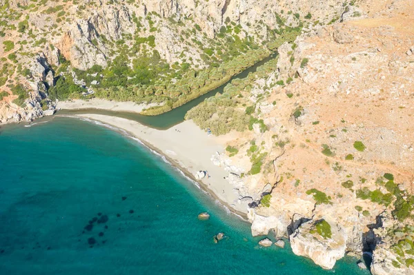 Bu manzara fotoğrafı Avrupa 'da, Yunanistan' da, Girit 'te, Preveli' de, Akdeniz kıyısında, yazın çekildi. Dağın eteğinde kumlu bir sahil görüyoruz. Güneşin altında, yeşil bir palmiye koruluğunun yanında..