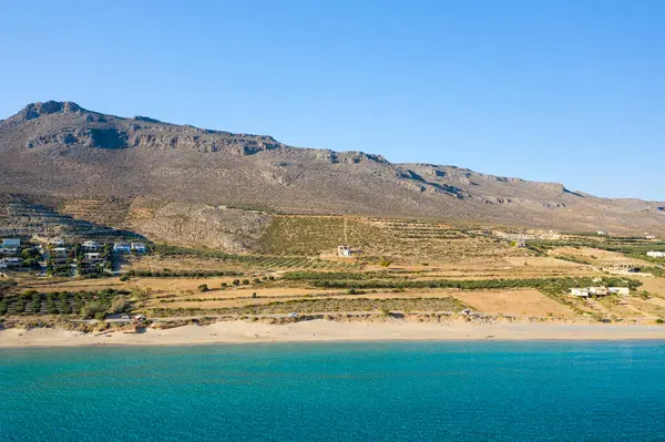 This landscape photo was taken, in Europe, in Greece, in Crete, towards Zakros, At the edge of the Mediterranean Sea, in summer. We see the fine sandy beach of Ambelou at the foot of the mountains, under the sun.