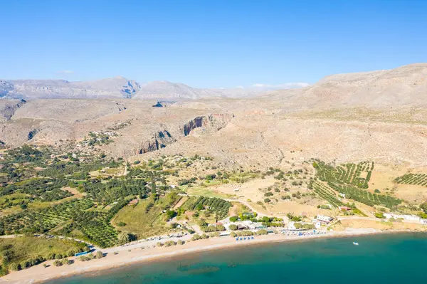 This landscape photo was taken, in Europe, in Greece, in Crete, in Kato Zakros, By the Mediterranean sea, in summer. We see the fine sandy beach at the foot of the arid mountains, under the sun.