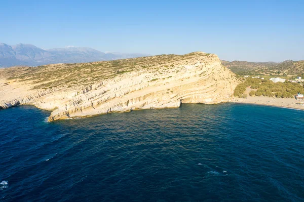 This landscape photo was taken, in Europe, in Greece, in Crete, in Matala, At the edge of the Mediterranean Sea, in summer. We see the hippie caves above the sandy beach, under the sun.