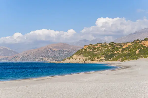 This landscape photo was taken, in Europe, in Greece, in Crete, towards Rethymno, At the edge of the Mediterranean Sea, in summer. We see Triopetra Beach and the surrounding mountains, under the sun.