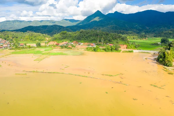 This landscape photo was taken, in Asia, in Vietnam, in Tonkin, in Dien Bien Phu, in summer. We see a traditional village on the edge of a lake and flooded rice fields in the middle of the mountains, under the Sun.
