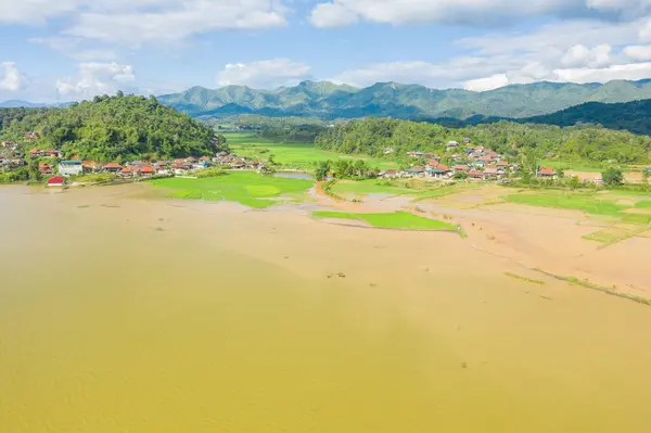 This landscape photo was taken, in Asia, in Vietnam, in Tonkin, in Dien Bien Phu, in summer. We see a traditional village on the edge of a lake and flooded rice fields in the middle of the mountains, under the Sun.