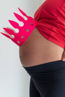 Hamile bir kadının göbeğinde canlı pembe bir taç var. Anneler Queens 'in ilham kaynağıdır. Hamilelik, annelik, annelik, spor ve sağlık konsepti. Parlak bir arkaplan ile yakın plan