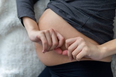 Hamile kadın göbeğinde kalp şekli oluştururken yan yatıp dinleniyor. Hamilelik acısı ve yorgunluğu yüzünden dinlenen bir kadın. Annelik, hamilelik kavramı. Yan görünüm, yakın çekim