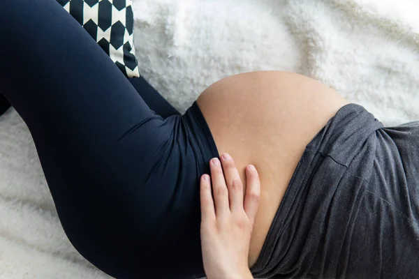 stock image  Pregnant woman lying on her side and touching her back with shown belly while using a pillow between her knees. Woman resting due to pregnancy pain and tiredness. Maternity, pregnancy concept. Above.