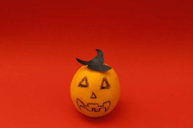 Turuncu, kırmızı arka planda Cadılar Bayramı balkabağına benziyor. Korkunç bir meyve.