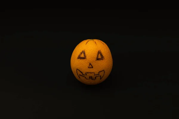 stock image Orange looks like a Halloween pumpkin on a black background, scary fruit