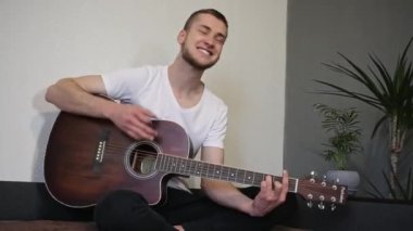 Bir adam yüzünde bir gülümsemeyle gitar çalar.