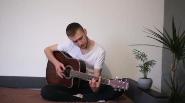 Adam kanepede gitar çalıyor.